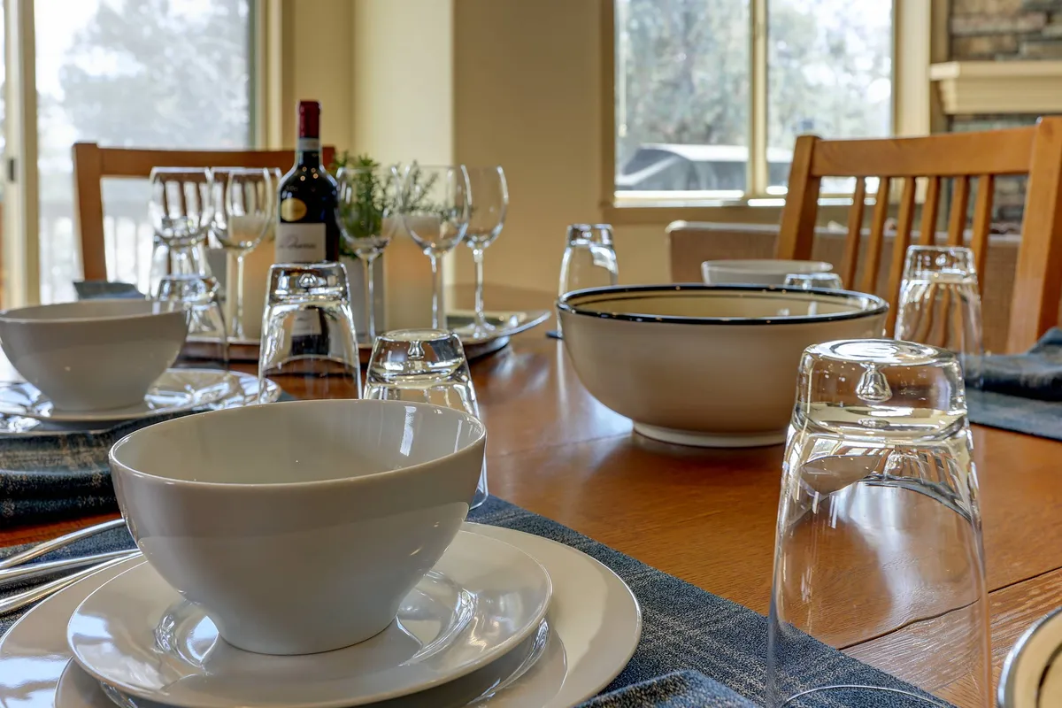 A stylish interior with a dining table elegantly set with dinnerware, wine bottles, and glasses, exuding a sense of celebration and togetherness. The mood is warm and lively, inviting shared stories and camaraderie.