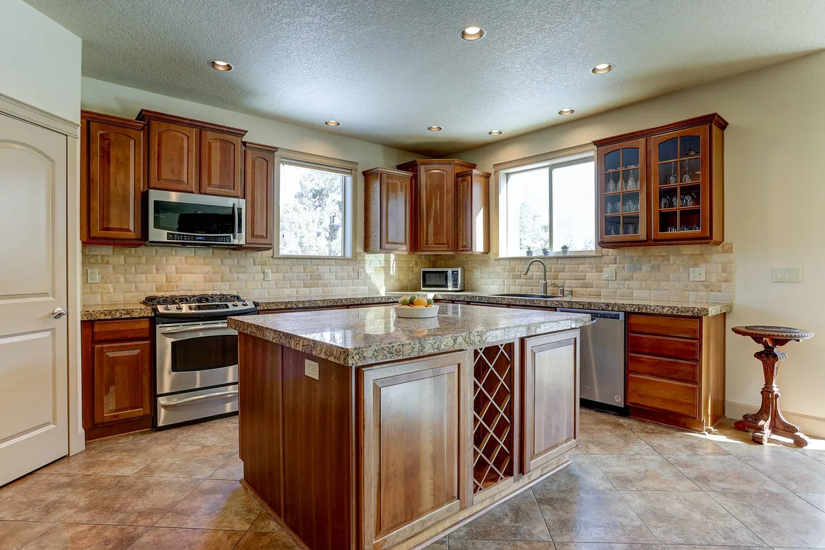 A gourmet kitchen with a large granite island, wooden cabinetry, and ample natural light from large windows. The countertops and spacious layout are perfect for group cooking, preparing snacks, and enjoying family gatherings.