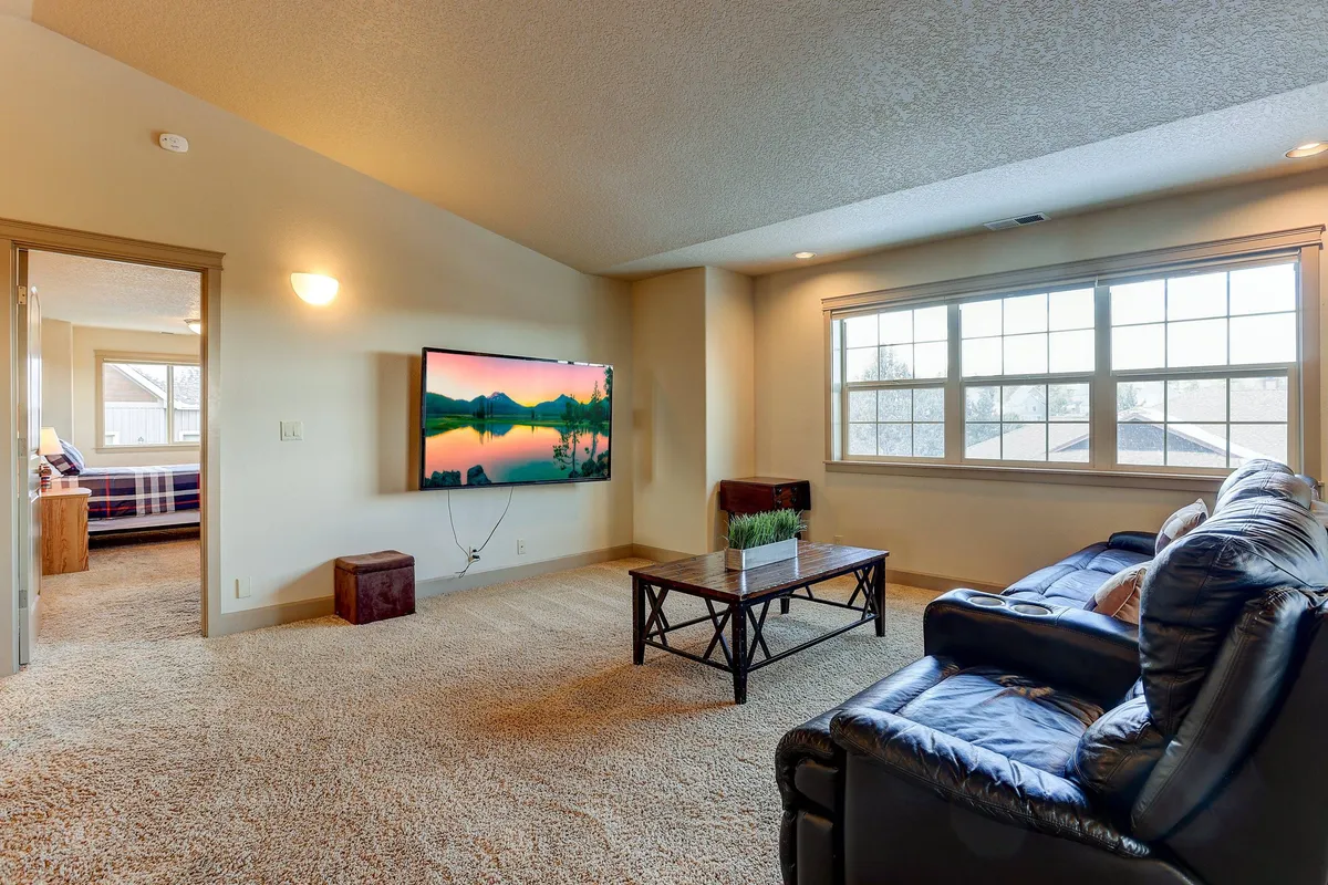 A cozy interior space with a sofa, coffee table, large TV, and a wide window. The scene invites relaxation, watching movies or sports, and hanging out with family or friends after a day of activities.