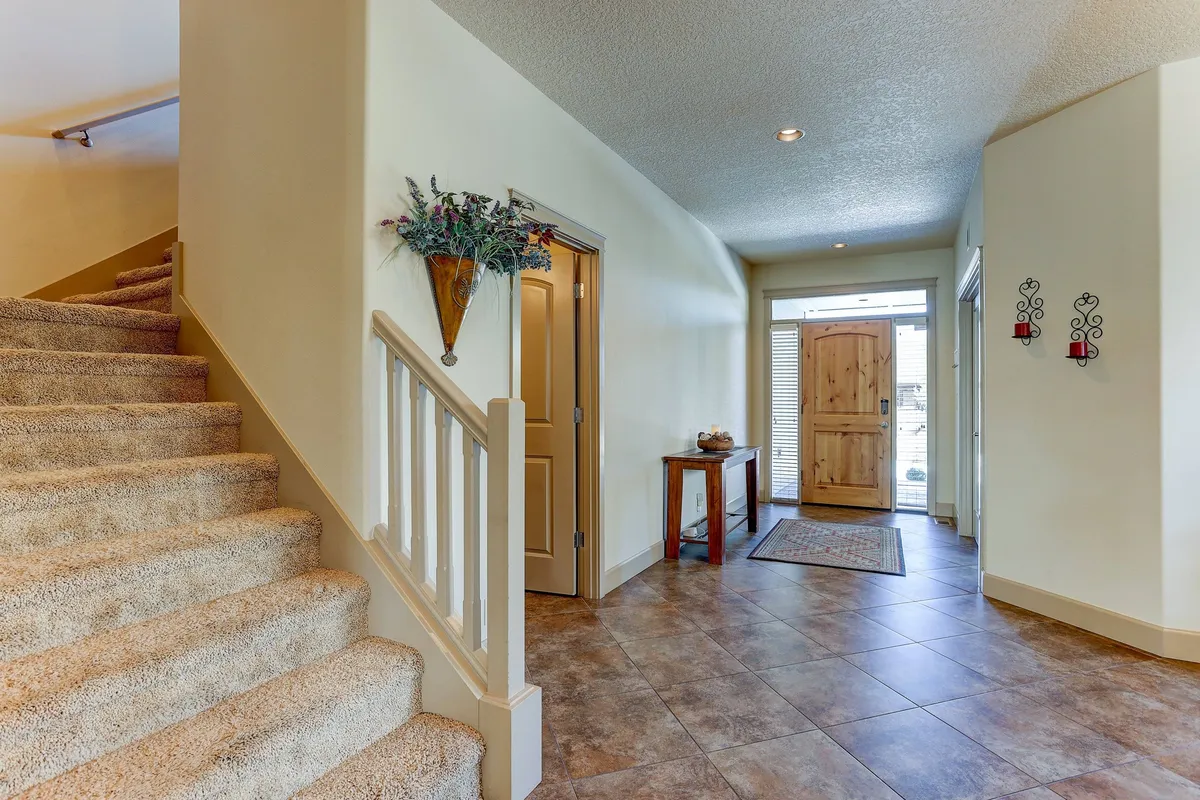 Shows the home's welcoming entryway with a staircase, front door, entry table, and decorative wall accents. The space feels warm and inviting, hinting at the home's open, family-friendly atmosphere from the very first step inside.