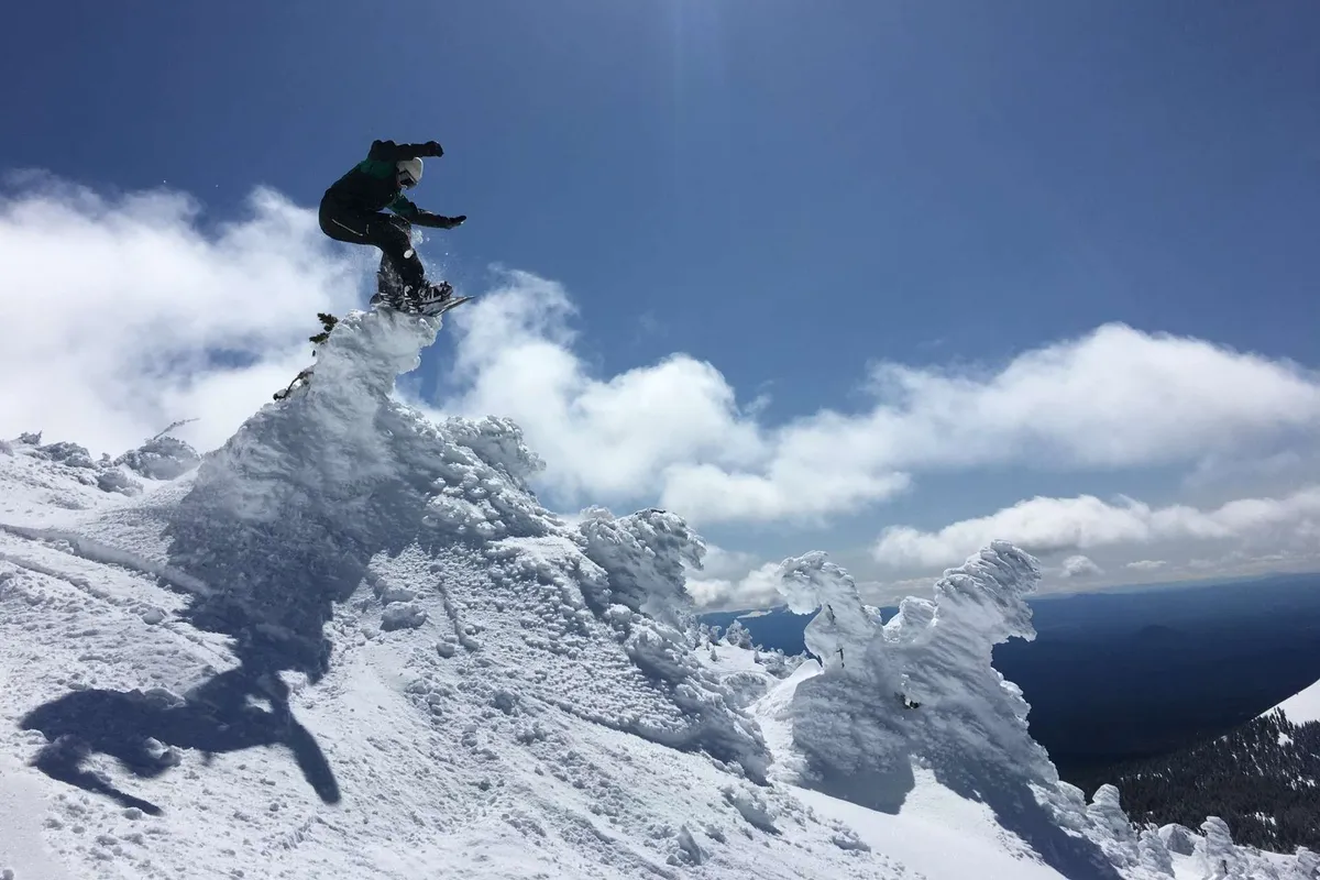A snowboarder is caught mid-air against a backdrop of a snow-covered peak and dramatic clouds. The energy and excitement of winter sports are palpable, highlighting the thrilling opportunities the region offers during the snowy season.
