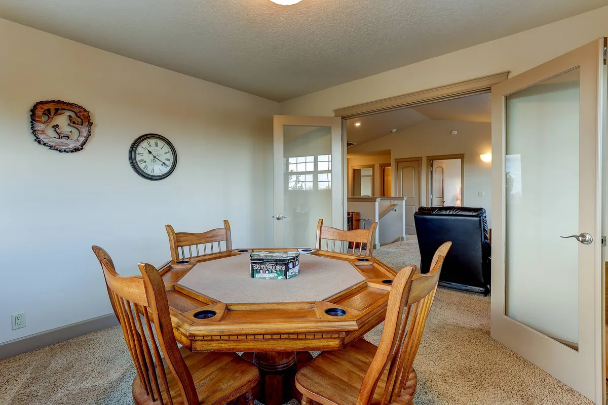 An inviting room featuring an octagonal game table surrounded by wooden chairs, a wall clock, and framed wall art. The atmosphere is comfortable and social, ideal for board games or card tournaments, with plenty of space for group gatherings.