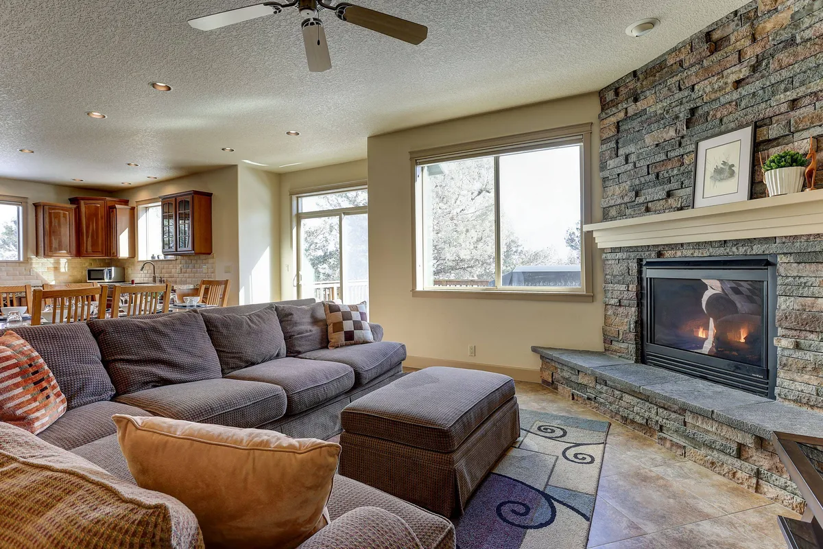 Features a comfortable sectional sofa arranged around a fireplace, with large windows letting in natural light. The room is designed for group gatherings, relaxation, and cozy fireside chats, accommodating multiple generations with its spacious, inviting layout.